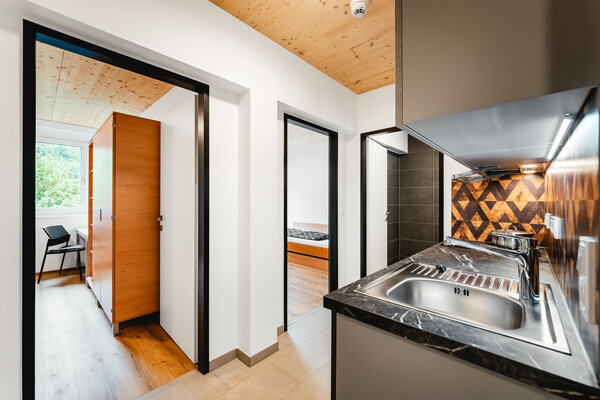 Gesamtsicht in ein Doppelstudio International Student Residence der HOK vom Eingang aus: Flur und eine modernen Küche im Vordergrund. Im Hintergrund blickt man in zwei Studierendenzimmer. mit Bett und Schreibtisch. | © HOK