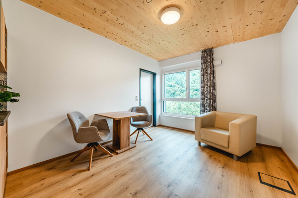 Ein moderner Raum mit Holzfußboden und Holzdecke. Im Raum befinden sich ein Tisch mit zwei Stühlen sowie ein großes Fenster mit Blick auf eine grüne Landschaft. | © HOK