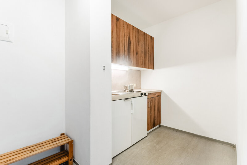 Eine kleine Küchenzeile in einem Doppelstudio in Haus A der Internation Student Residence mit Holzfronten an den Oberschränken, einer Edelstahlspüle und weißen Unterschränken.