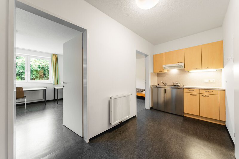 Eine kleine Wohnung mit einer modernen Küche. Im Hintergrund sind zwei Räume sichtbar.