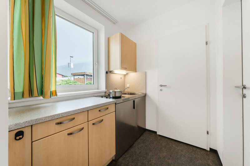 Eine gut beleuchtete Küche mit modernen Annehmlichkeiten. Über der Spüle befindet sich ein Fenster, das Tageslicht hereinlässt und einen Blick nach draußen bietet.