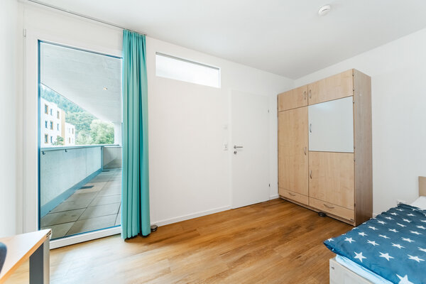 Ein modernes, gut beleuchtetes Schlafzimmer mit einem großen Schrank und einem Fenster, das zu einem Balkon führt. Rechts vom Schrank befindet sich ein Bett. | © HOK