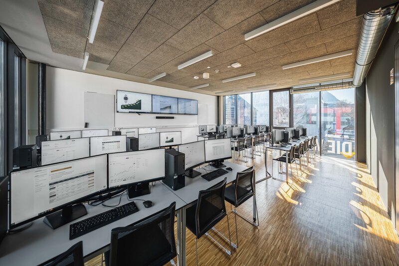 Gesamtansicht des Finance Lab der HOK mit mehreren Computerarbeitsplätzen und großen Bildschirmen an der Wand.