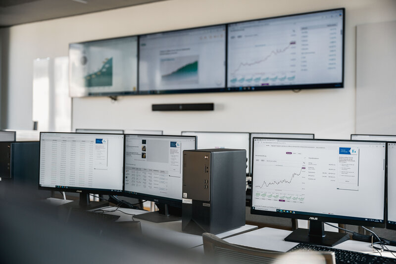 Computerarbeitsplätze im Finance Lab der HOK mit Diagrammen und Finanzdaten auf Monitoren.