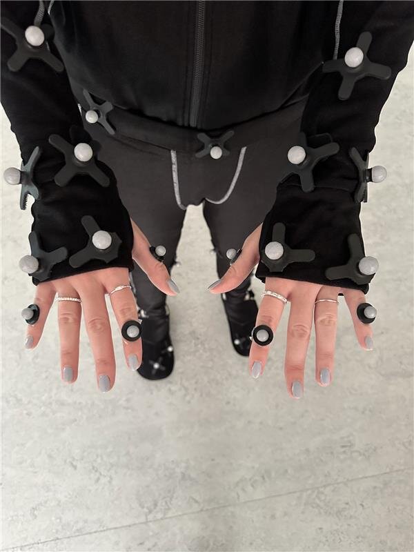 Detailaufnahme der Hände einer Person im Motion-Capture-Anzug mit Reflektionsmarkern und Fingertrackern im MoCap-Lab der HOK