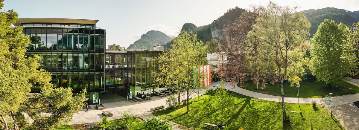Panoramaaufnahme des Campus der HOK mit moderner Glasfassade, Grünflächen und Bergkulisse