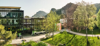 Panoramaaufnahme des Campus der HOK mit moderner Glasfassade, Grünflächen und Bergkulisse