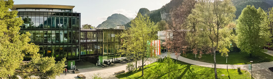 Panoramaaufnahme des Campus der HOK mit moderner Glasfassade, Grünflächen und Bergkulisse