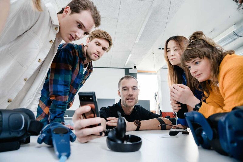 Gruppe von Studierenden und Dozent diskutiert über Smartphone-Interface im Web Lab der HOK.