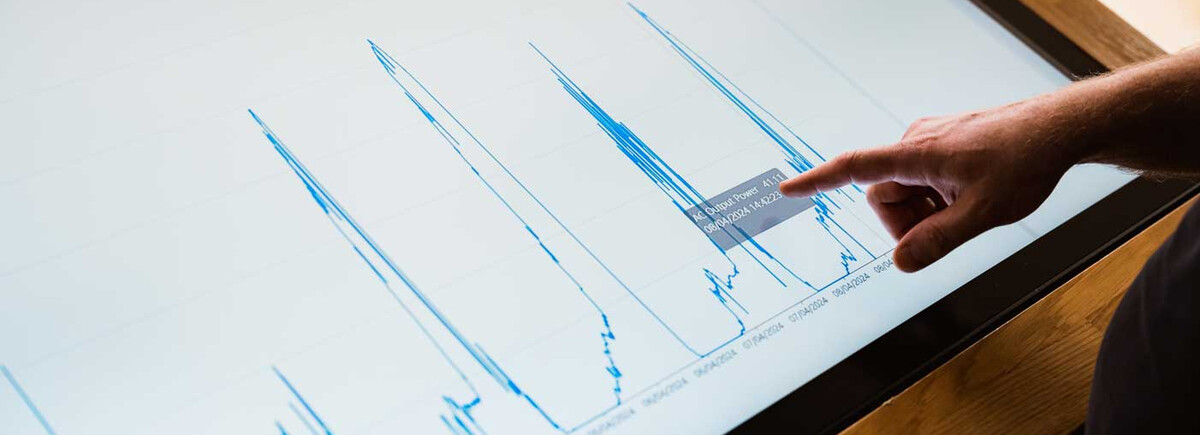 Finger zeigt auf Energiediagramm mit Leistungsdaten auf Touchscreen im Sustain & Estate Lab der HOK.