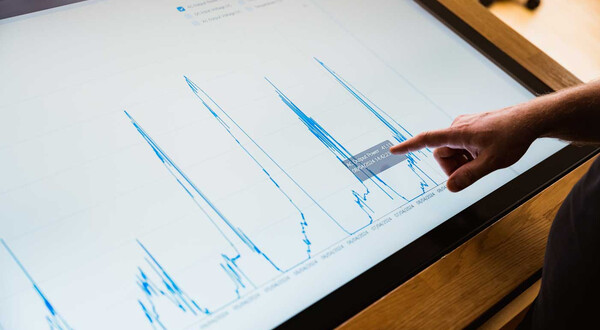 Finger zeigt auf Energiediagramm mit Leistungsdaten auf Touchscreen im Sustain & Estate Lab der HOK.