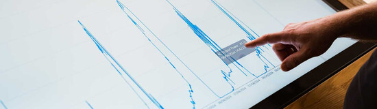Finger zeigt auf Energiediagramm mit Leistungsdaten auf Touchscreen im Sustain & Estate Lab der HOK.
