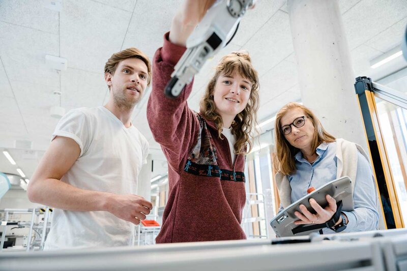 Drei Personen beobachten und steuern einen Roboterarm im Automation Lab mit einem Tablet.