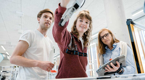 Drei Personen beobachten und steuern einen Roboterarm im Automation Lab mit einem Tablet.