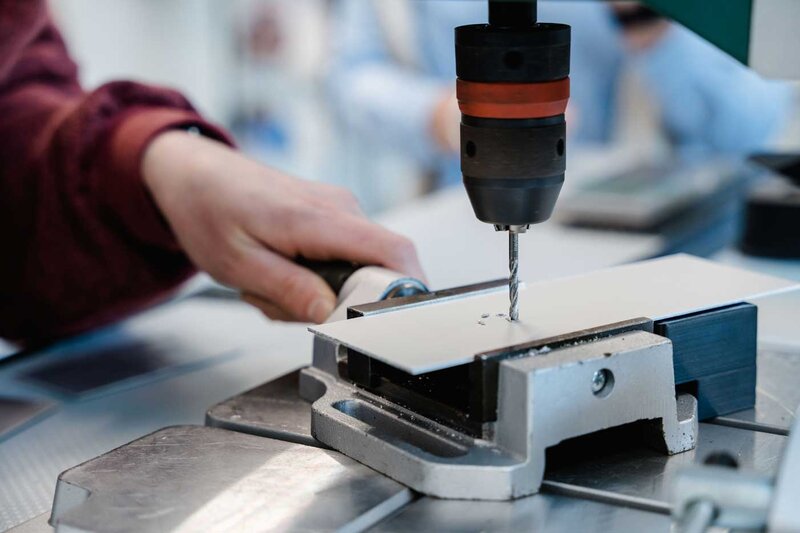 Bohrmaschine im Lean Lab der HOK bohrt präzise Löcher in ein Metallblech während einer Übung zur Produktionstechnik.
