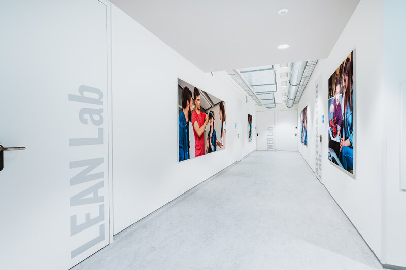 Heller Flur im Laborbereich der HOK mit Wandgrafiken und Beschriftungen der Labore, darunter das Lean Lab.