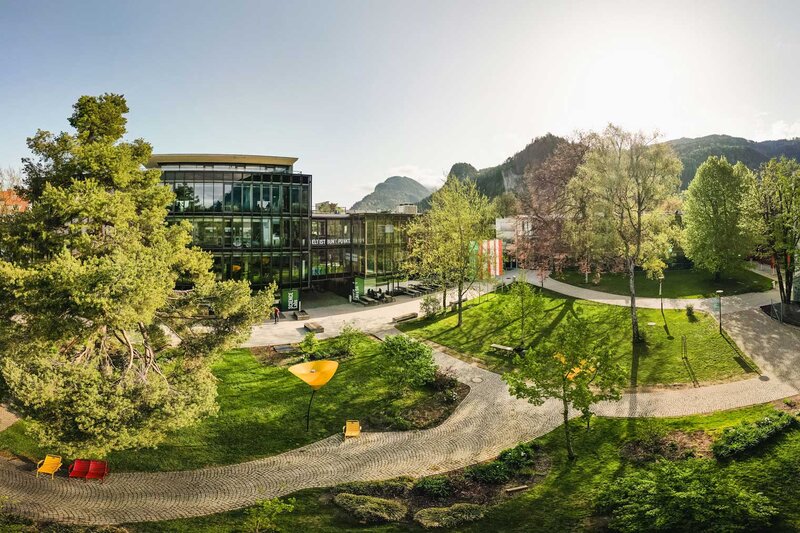 Weitläufiger Campus der HOK mit Grünflächen, modernen Gebäuden und Bergpanorama