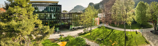 Weitläufiger Campus der HOK mit Grünflächen, modernen Gebäuden und Bergpanorama