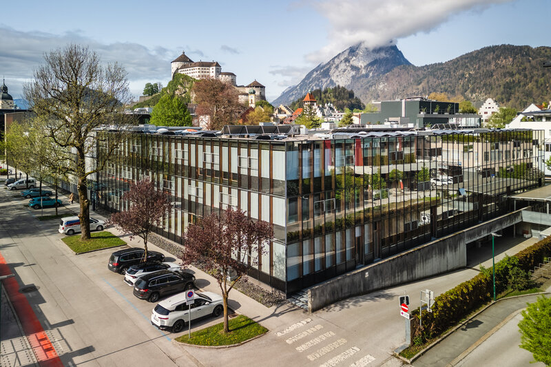 Luftaufnahme des modernen Hauptgebäudes der HOK mit Festung und Bergen im Hintergrund