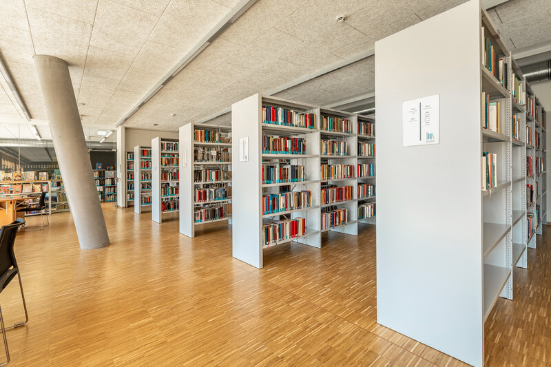 Lesesaal der kubi am Campus der HOK mit Bücherregalen, Holzfußboden und sichtbarer Betondecke.