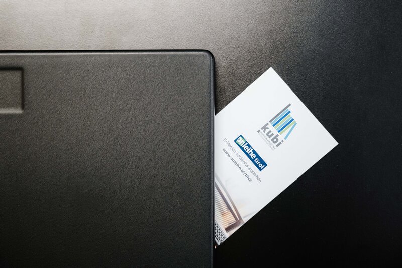 Bibliotheksausweis der kubi  mit Logo und Text 'kubi', 'meine tirol', teilweise sichtbar neben schwarzem Laptop auf dunklem Untergrund