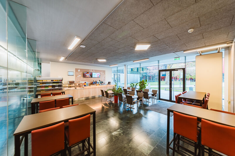 Innenansicht der Cafeteria der HOK mit Sitzbereichen, Theke und Ausblick auf den Campus
