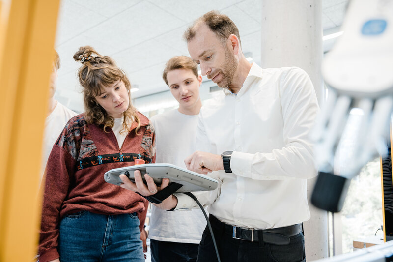 Lehrender erklärt Studierenden die Steuerung einer Automatisierungsanlage über ein Tablet im Labor der HOK.