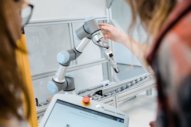 Studierende im Lean Lab der HOK arbeiten mit einem kollaborativen Roboterarm und testen dessen Greifmechanismen in der Fertigungssimulation.