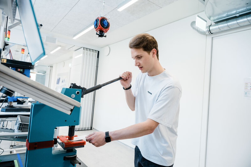 Student bedient im Lean Lab der HOK eine Stanzmaschine und führt präzise Fertigungsschritte im Rahmen eines Produktionsprozesses durch.