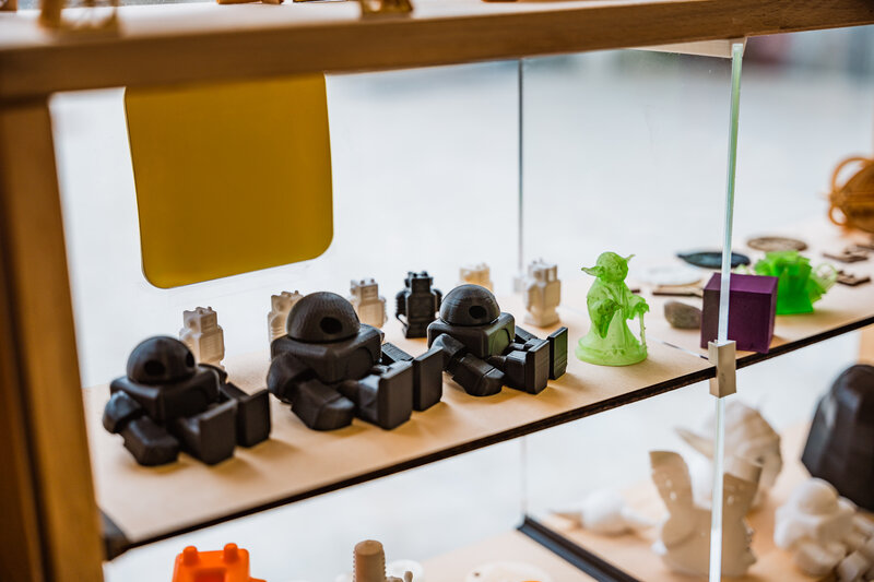 Vitrine im Makers Lab der HOK mit farbigen 3D-Druckmodellen, Figuren und technischen Miniaturen.