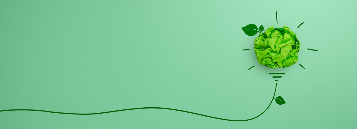 Grüne Glühbirne aus Papier mit Blattelementen auf grünem Hintergrund – Sinnbild für nachhaltige Innovation und kreative Energiekonzepte.