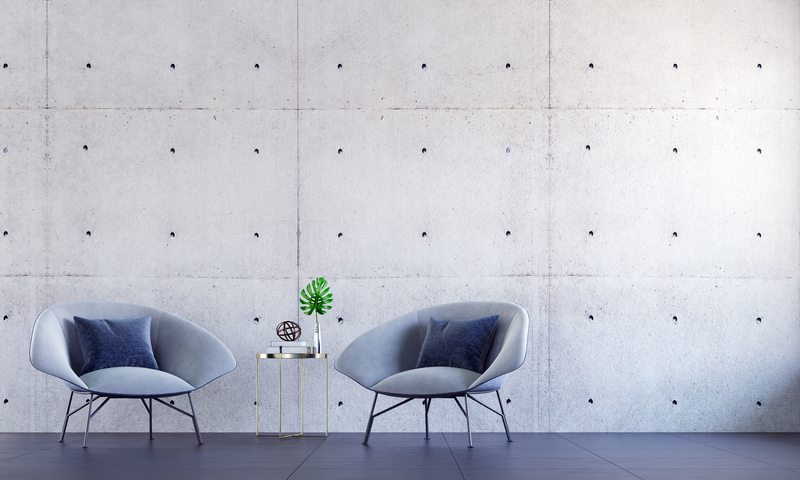 Zwei moderne Stühle mit kleinem Beistelltisch vor einer Betonwand – stilvolles Ambiente für Gespräche und Austausch in entspannter Atmosphäre.