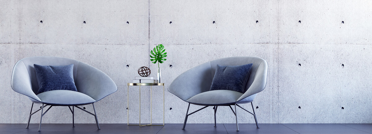 Zwei moderne Stühle mit kleinem Beistelltisch vor einer Betonwand – stilvolles Ambiente für Gespräche und Austausch in entspannter Atmosphäre.