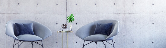 Zwei moderne Stühle mit kleinem Beistelltisch vor einer Betonwand – stilvolles Ambiente für Gespräche und Austausch in entspannter Atmosphäre.