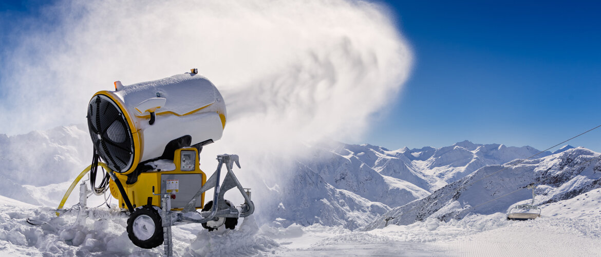 Schneekanone erzeugt künstlichen Schnee auf einer Bergpiste mit Alpenpanorama – Sinnbild für technologische Innovation und effiziente Ressourcennutzung im Wintertourismus. | © Adobe.Stock.Gerold H. Waldhart