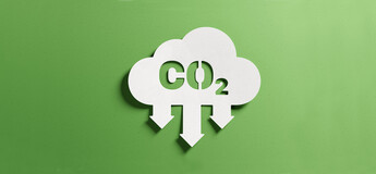 Weiße Wolke mit CO₂-Symbol und nach unten gerichteten Pfeilen auf grünem Hintergrund, sinnbildlich für Emissionsanalyse und Reduktion von Treibhausgasen.