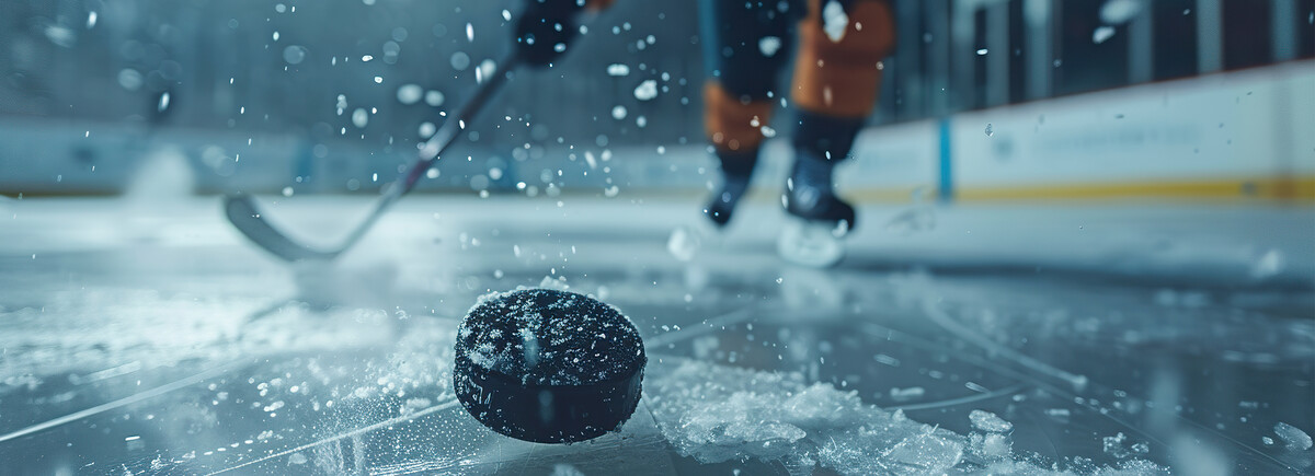 Nahaufnahme eines Eishockey-Pucks auf dem Eis mit Spieler im Hintergrund – Symbol für Dynamik, Präzision und sportlichen Wettkampf.