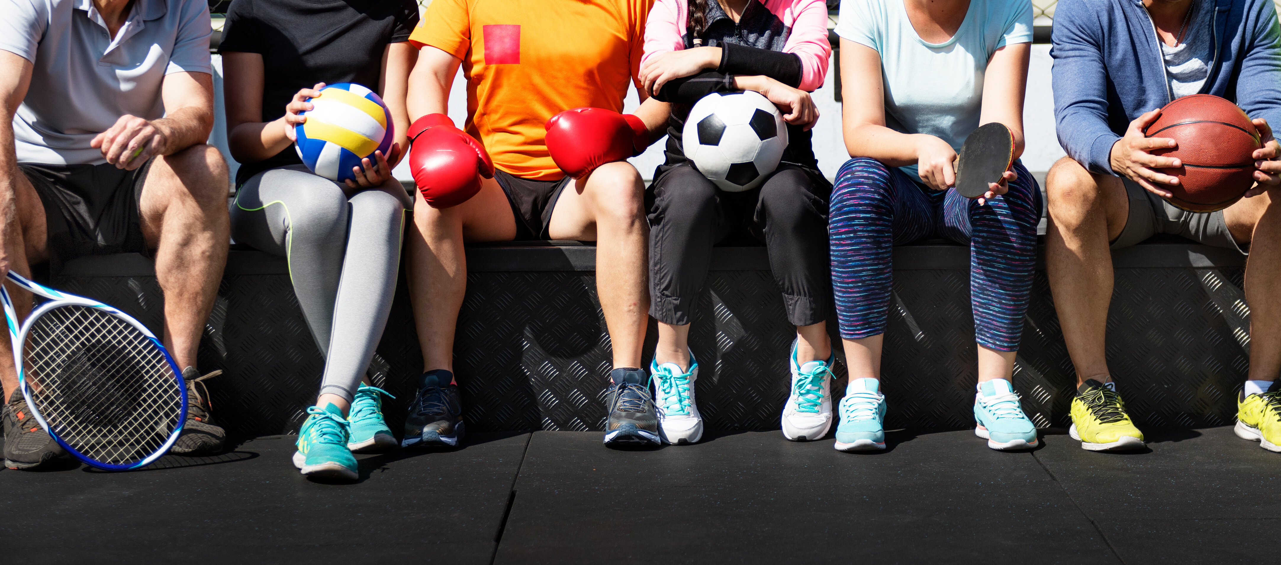 Mehrere Personen mit unterschiedlichen Sportutensilien sitzen nebeneinander – Sinnbild für Vielfalt, Gemeinschaft und die verbindende Kraft des Sports. | © AdobeStock.Rawpixel.com