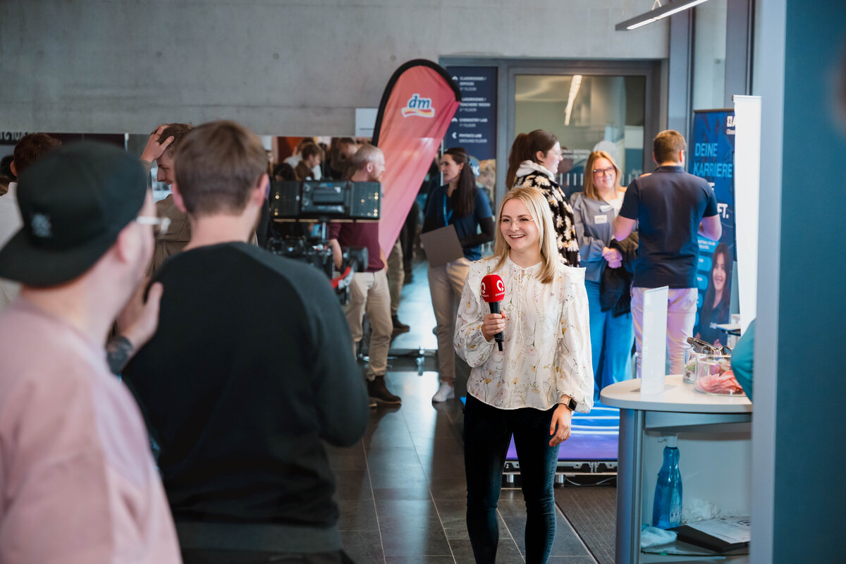 Frau mit Mikrofon spricht auf der Karrieremesse Meet & Match in eine Fernsehkamera