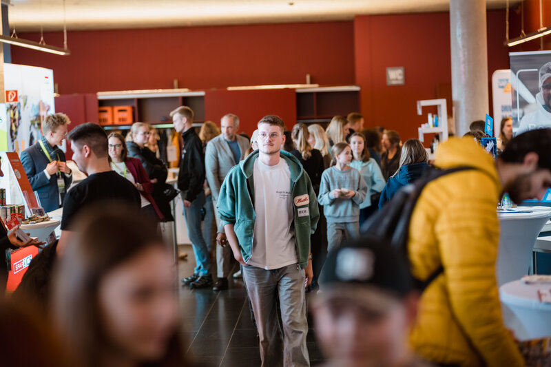 Menschen gehen durch einen großen Raum voller Besucher:innen auf der Karrieremesse Meet & Match.
