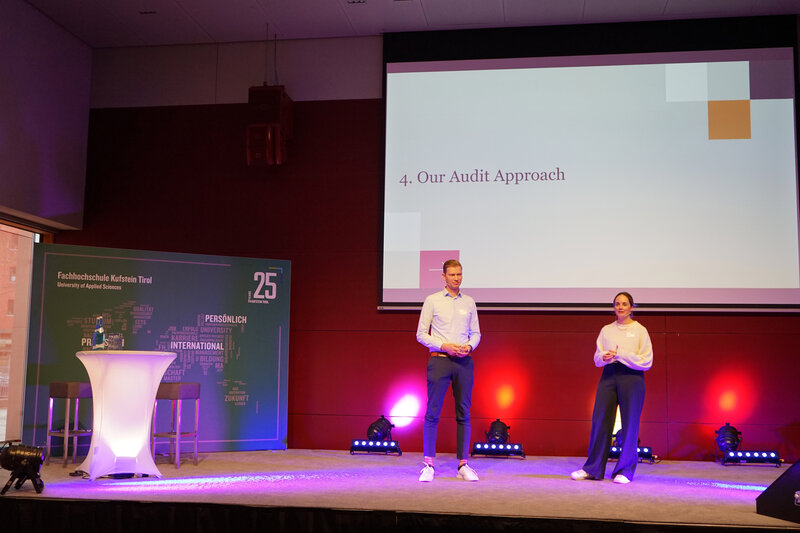 Carina Allmann und Eduard Obernauer präsentieren beim 23. PQM-Dialog an der HOK auf einer Bühne vor einer Projektion mit dem Titel „Our Audit Approach“.