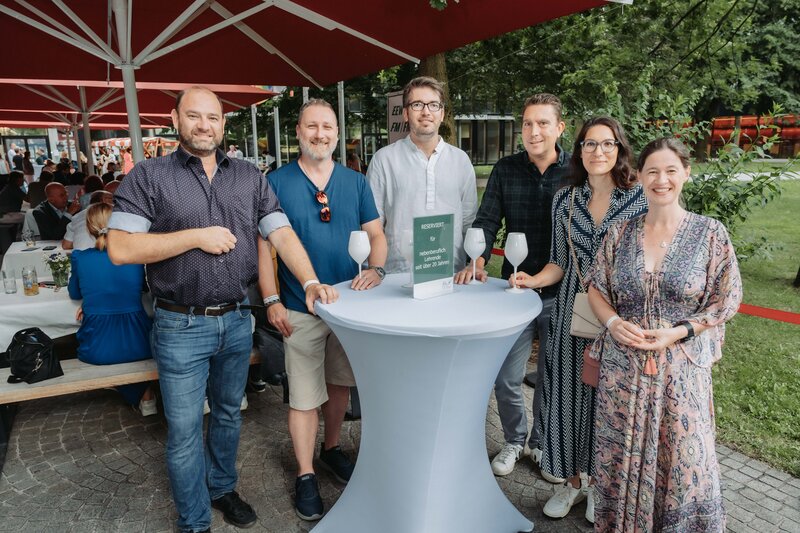 Mehrere Gäste stellen sich lächelnd in Zweierreihen für das Foto auf.