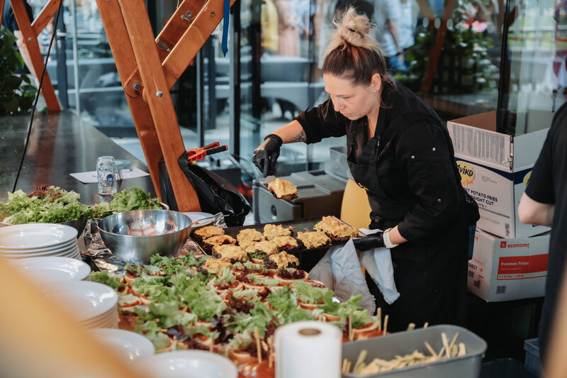 In schwarzer Berufskleidung arbeitet die Catering-Mitarbeiterin am Burger-Station. 