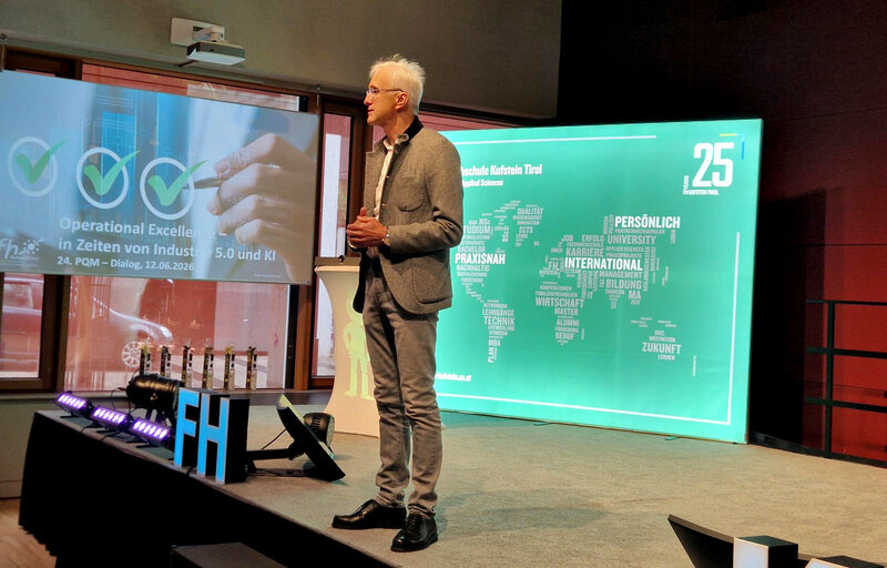 Professor Martin Adam hält die Begrüßungsrede beim 24. PQM-Dialog 2026 an der HOK auf der Bühne vor einer Präsentation zu Operational Excellence.