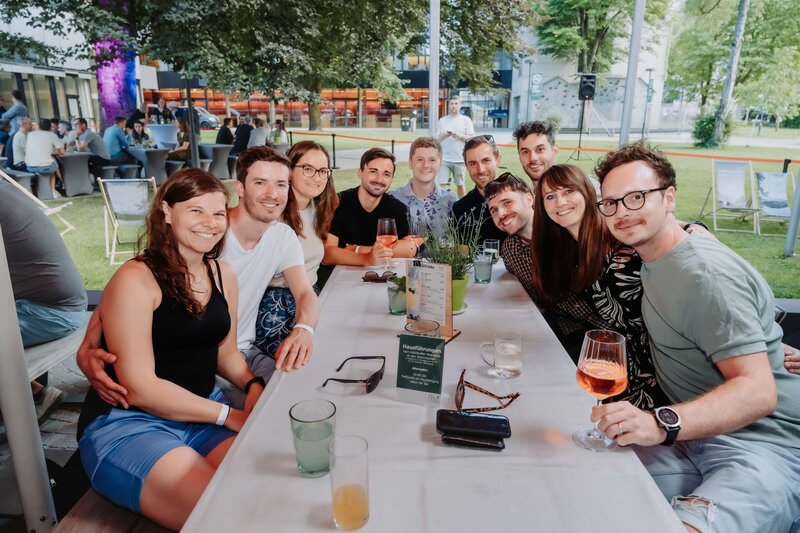Teilnehmerinnen und Teilnehmer des HomeComing 2026 sitzen gemeinsam an einem Tisch im Stadtpark Kufstein.