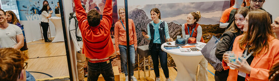 Ein Mann macht Klimmzüge an einem Klettergriffbrett vor dem Oberalp Messestand, während andere Besucher zuschauen und interagieren.