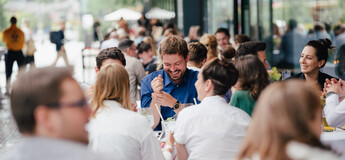 Eine große Gruppe von Personen unterhält sich und lacht beim Homecoming-Event im Außenbereich.