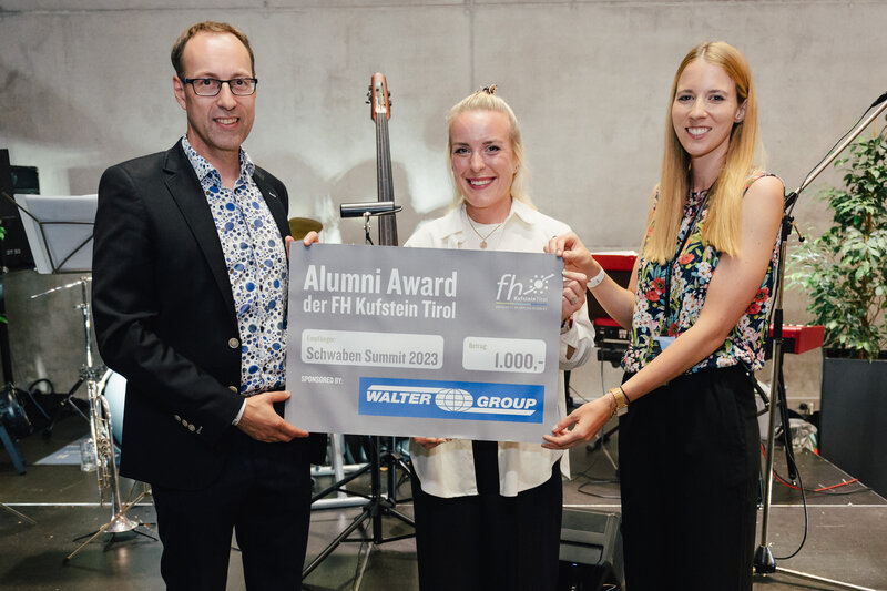 Zwei Personen übergeben der Dame den Alumni Award im Rahmen des HomeComing Events an der HOK.