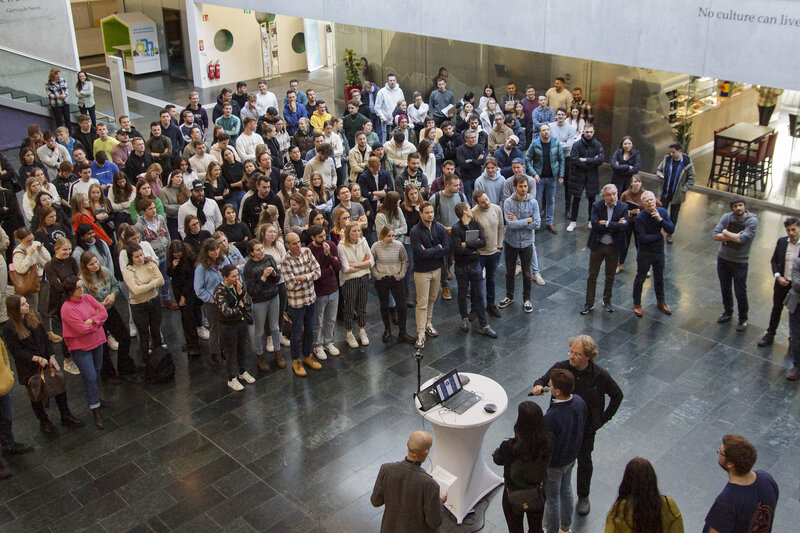 Eine große Gruppe von Menschen versammelt sich in der modernen Aula der HOK.