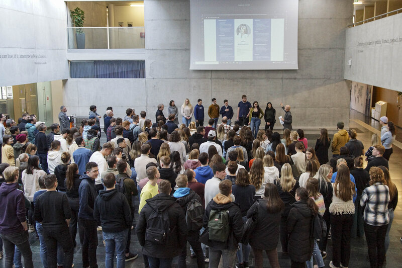 Eine große Gruppe von Menschen versammelt sich in der modernen Aula der HOK.